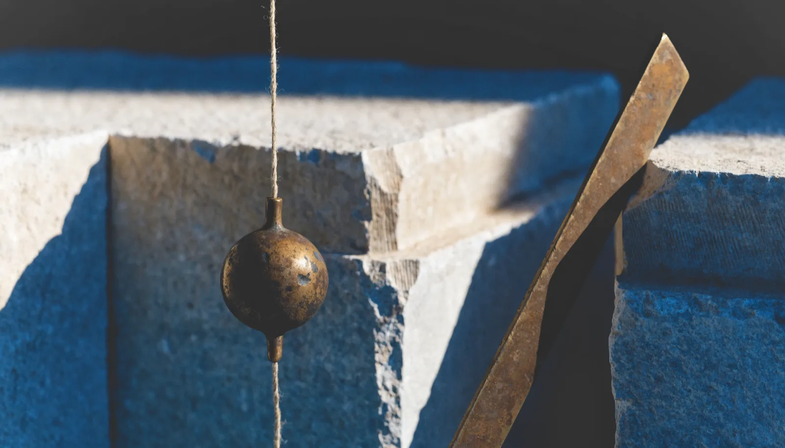 A bronze plumb bob hanging still beside a set square against dressed stone.